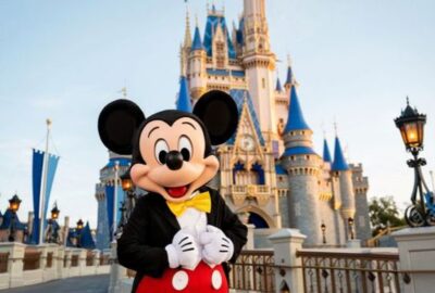 Mickey Mouse de fraque preto, gravata-borboleta amarela e calça vermelha posa em frente ao castelo da Cinderela, no Magic Kingdom
