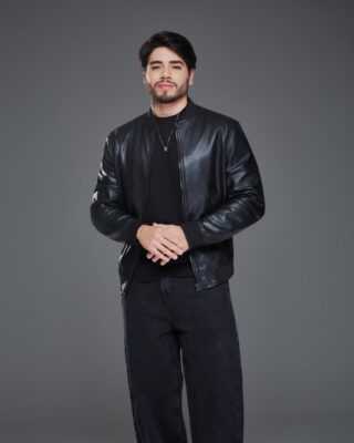 O cantor Thiago Freitas, de jaqueta de couro preta, camiseta e calça escuras, posa com as mãos juntas em fundo cinza